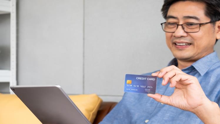 A man holding a credit card and sitting on a sofa with a laptop.